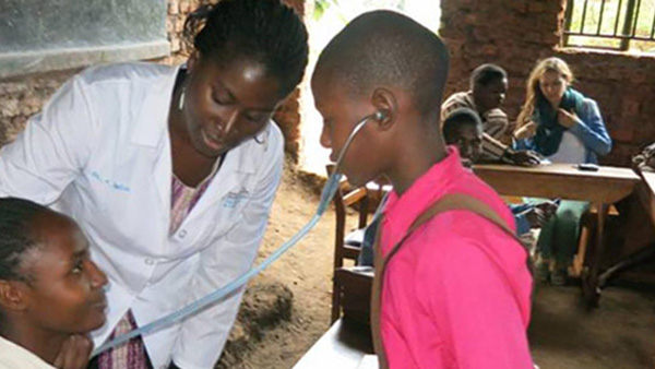 In a clinic in Africa, a doctor lets a young boy listen to another patient's heartbeat
